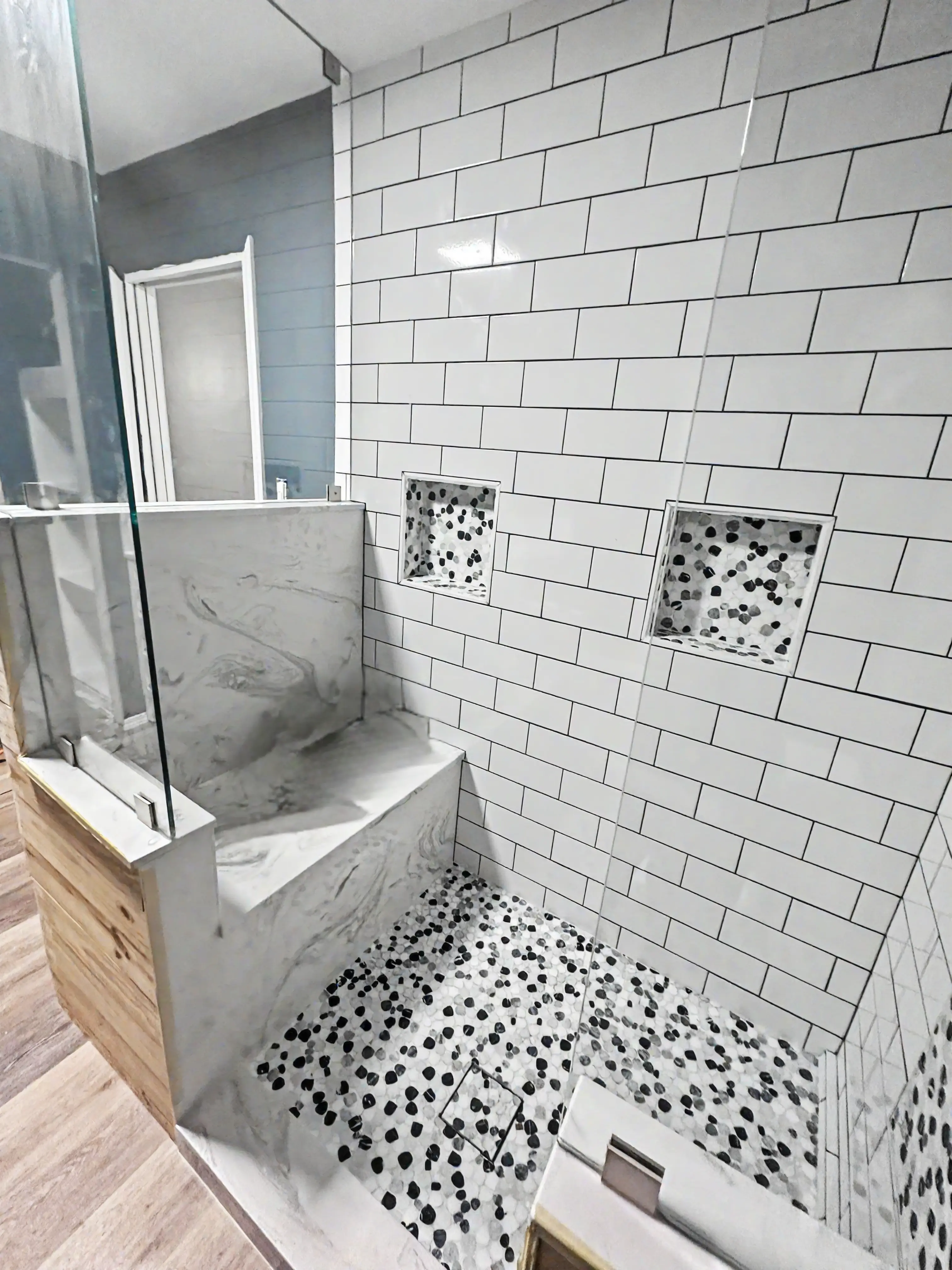 Custom tile shower installation with subway tile walls, pebble stone floor, built-in niches, and bench seating